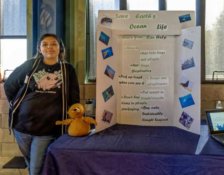 A student stands next to a poster board that says, “Save Earth’s Ocean Life,” and multiple conservation tips.