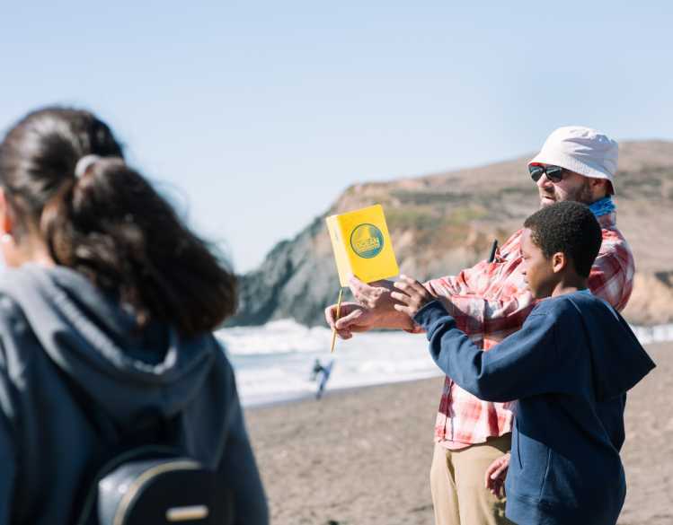 An adult and a child hold a yellow booklet on the beach.