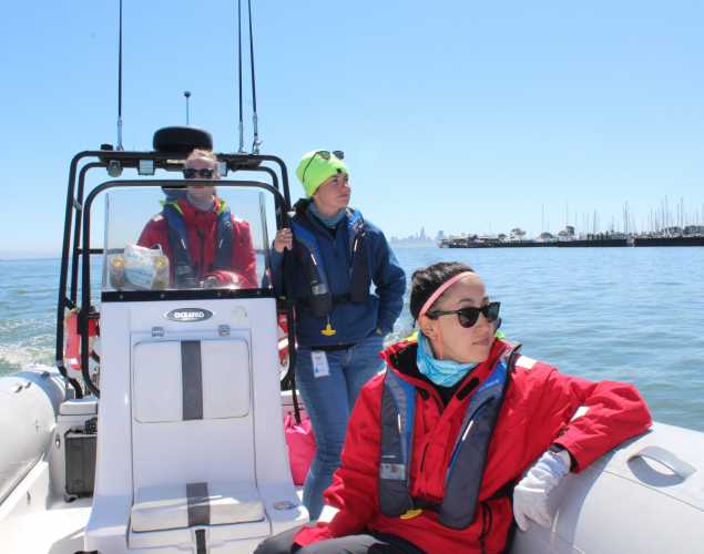Three researchers on a boat looking for whales with Bekah Lane in the center