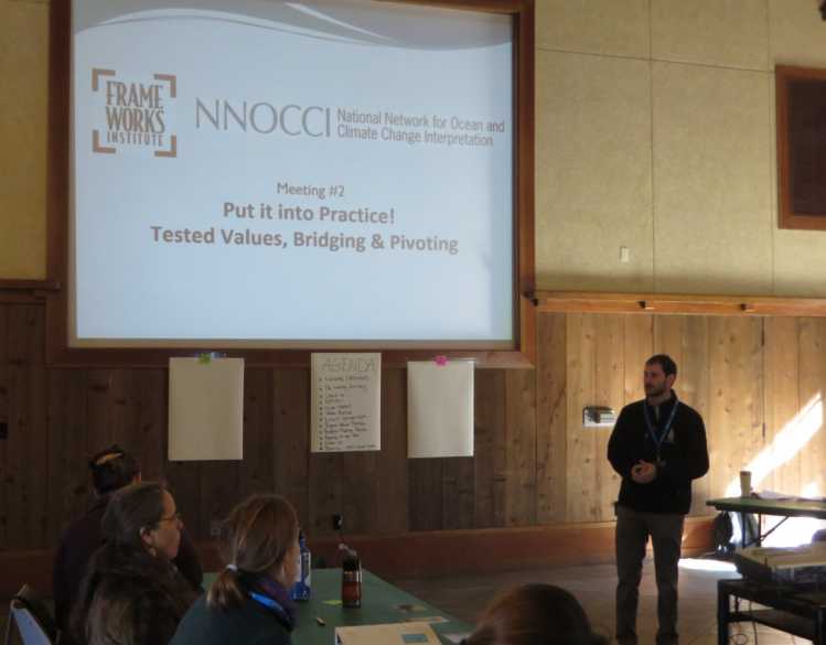 A presenter stands in front of a screen that says “NNOCCI: Putting it into practice! Tested values, bridging & pivoting.”