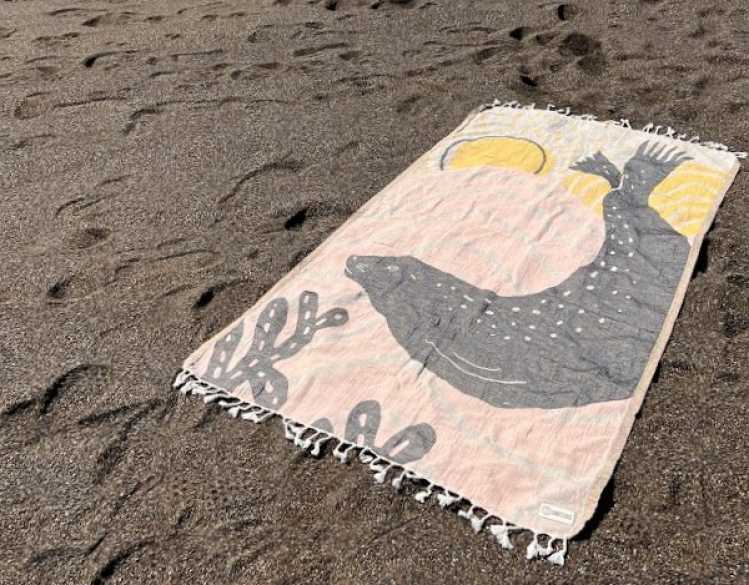 peach-colored lightweight beach towel with gray harbor seal and yellow sun design