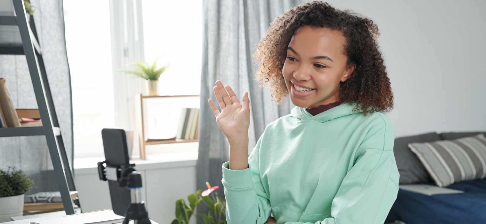 student smiling and waving at phone camera