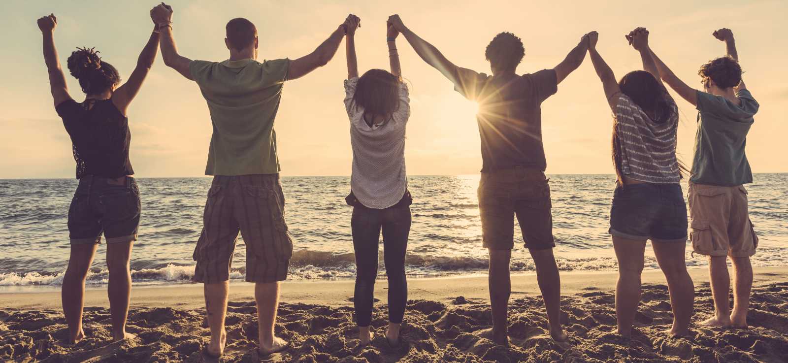 group of young people on the beach with hands clasped and raised