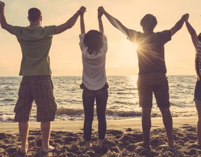 group of young people on the beach with hands clasped and raised